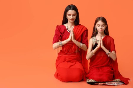 Photo for Mother with her daughter in sari praying on orange background. Divaly celebration - Royalty Free Image
