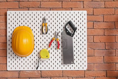 Pegboard with builder's tools on brick wall in workshop