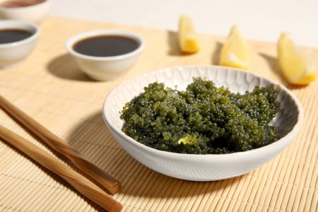 Foto de Cuenco con algas sanas, salsa de soja y rodajas de limón en la estera de bambú, primer plano - Imagen libre de derechos