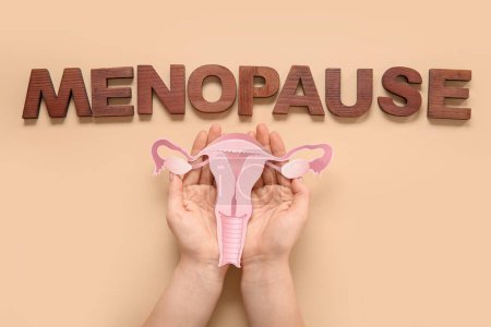 Woman with paper uterus and word MENOPAUSE on beige background