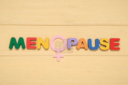 Palabra MENOPAUSE con símbolo de mujer sobre fondo de madera amarillo