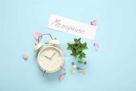 Word MENOPAUSE with alarm clock, pills and petals on blue background