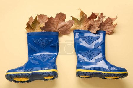 Foto de Botas de goma azules con hojas de otoño sobre fondo amarillo - Imagen libre de derechos