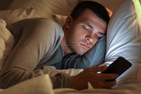 Junger Mann mit Handy schläft nachts im Bett, Nahaufnahme