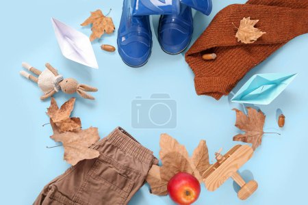 Foto de Marco hecho de botas de goma azules con suéter, pantalones, barcos de papel y hojas de otoño sobre fondo de color - Imagen libre de derechos