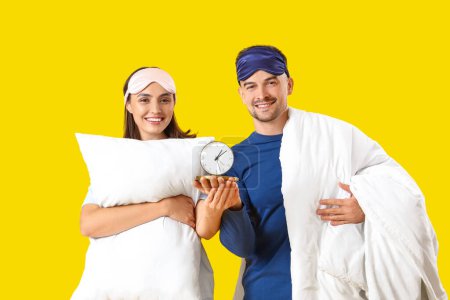 Photo for Young couple with pillow and alarm clock on yellow background - Royalty Free Image
