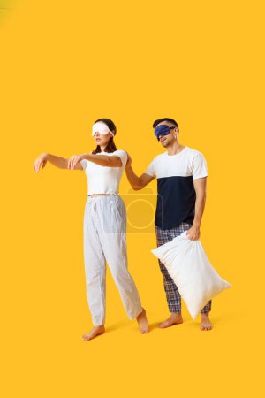 Téléchargez les photos : Jeune couple avec des masques de couchage et oreiller sur fond jaune - en image libre de droit