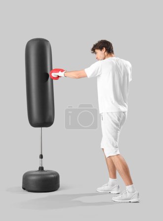 Téléchargez les photos : Jeune homme en boxe sportive avec sac de boxe sur fond gris - en image libre de droit