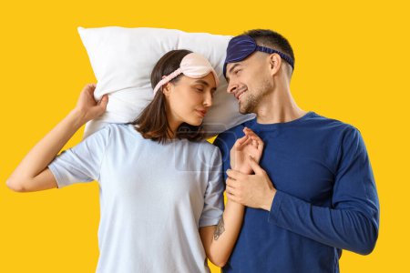 Téléchargez les photos : Jeune couple avec des masques de couchage et oreiller sur fond jaune - en image libre de droit