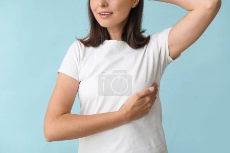 Foto de Mujer joven revisando su pecho sobre fondo azul, primer plano. Concepto de concienciación - Imagen libre de derechos