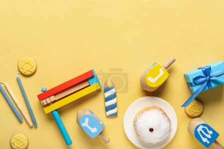 Photo for Hannukah composition with donut, rattle and dreidels on yellow table - Royalty Free Image