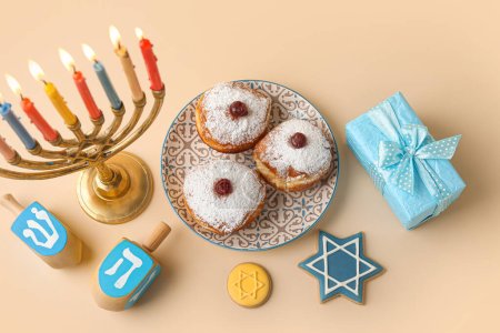 Photo for Menorah, dreidels, plate with donuts and gift box for Hanukkah celebration on beige background - Royalty Free Image