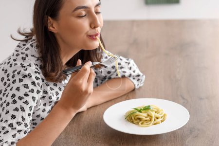 Foto de Mujer joven comiendo pasta sabrosa en la mesa en la cocina - Imagen libre de derechos