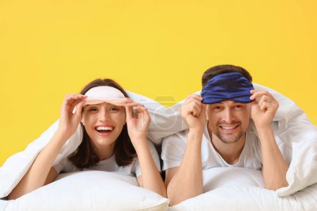 Téléchargez les photos : Jeune couple avec couverture et oreillers couchés sur fond jaune - en image libre de droit