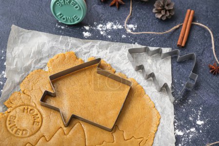 Foto de Masa cruda y cortadores para preparar sabrosas galletas de Navidad sobre fondo oscuro, primer plano - Imagen libre de derechos