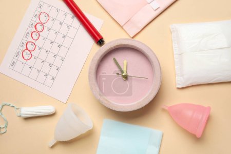 Komposition mit Wecker, Menstruationskalender und verschiedenen femininen Hygieneartikeln auf farbigem Hintergrund