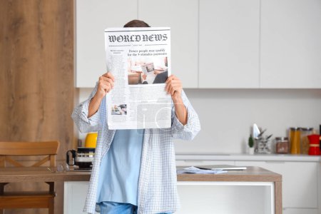 Young man with newspaper in kitchen