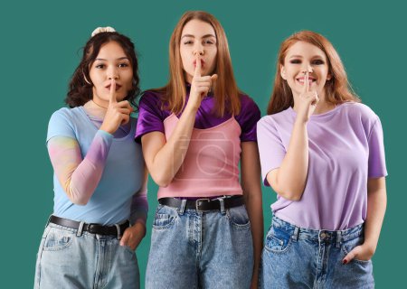 Photo for Young gossip women showing silence gesture on green background - Royalty Free Image