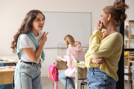 Photo for Female students gossiping about their classmate in classroom - Royalty Free Image