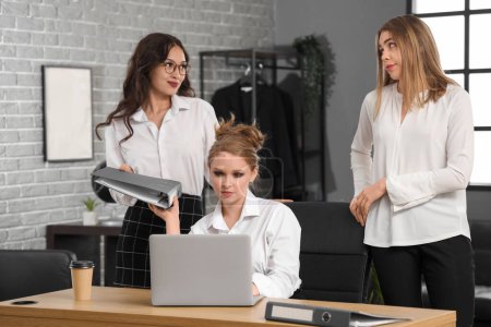 Photo for Young women gossiping behind colleague's back in office - Royalty Free Image