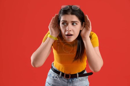Photo for Young gossip woman trying to hear something on red background - Royalty Free Image