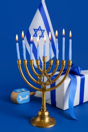 Téléchargez les photos : Menorah avec des bougies allumées, dreidel et cadeau pour Hanoukka célébration sur fond bleu - en image libre de droit