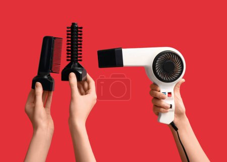 Téléchargez les photos : Mains féminines avec différents peignes et sèche-cheveux sur fond rouge. - en image libre de droit