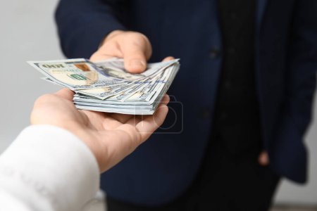 Young businessman giving bribe on light background, closeup