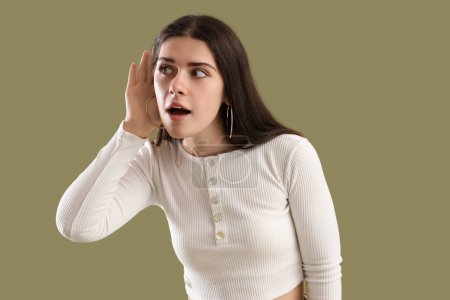 Téléchargez les photos : Jeune femme commérage essayant d'entendre quelque chose sur fond vert - en image libre de droit
