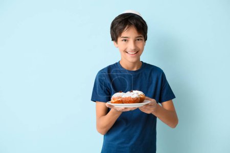 Photo for Little boy in kipa holding plate with tasty donuts on blue background. Hanukkah celebration - Royalty Free Image