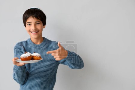 Photo for Little boy in kipa pointing at plate with tasty donuts on grey background. Hanukkah celebration - Royalty Free Image