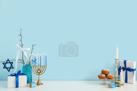 Armario blanco con menorah, sufganiyots, dreidels y cajas de regalo cerca de la pared azul. Hanukkah celebración