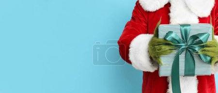 Téléchargez les photos : Créature en costume de Père Noël tenant cadeau de Noël sur fond bleu clair avec espace pour le texte - en image libre de droit