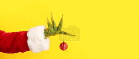 Photo for Green hairy hand with Christmas ball on yellow background with space for text - Royalty Free Image