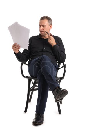 Téléchargez les photos : Acteur mature avec pipe fumeur lecture film script dans la chaise sur fond blanc - en image libre de droit