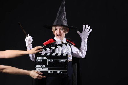 Téléchargez les photos : Petit acteur habillé en magicien et les mains avec claquement de film sur fond sombre - en image libre de droit