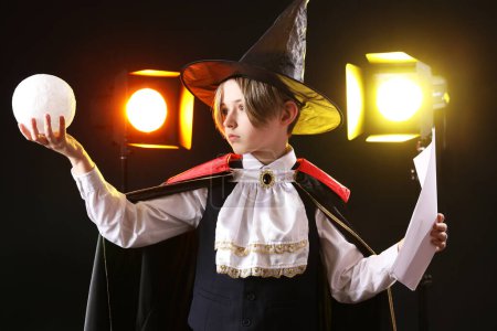 Téléchargez les photos : Petit acteur habillé en magicien avec scénario de film sur fond sombre - en image libre de droit