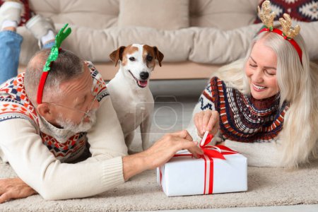 Foto de Feliz pareja madura con lindo perro y regalo en casa en la víspera de Navidad - Imagen libre de derechos