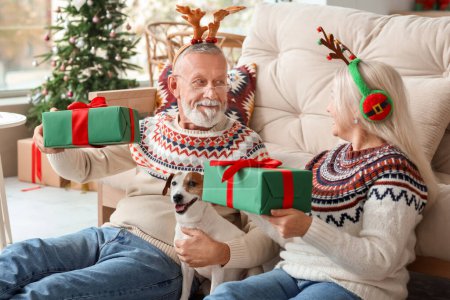 Foto de Feliz pareja madura con lindo perro y regalos en casa en la víspera de Navidad - Imagen libre de derechos