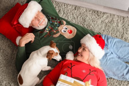 Foto de Feliz pareja madura con perro y regalo tumbado en casa en la víspera de Navidad, vista superior - Imagen libre de derechos