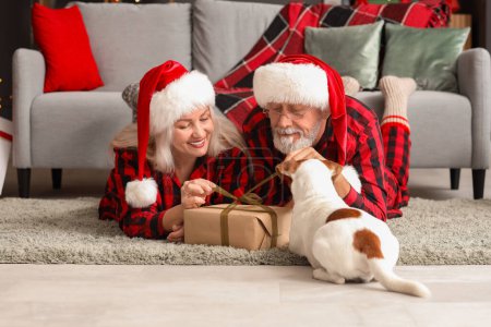 Foto de Feliz pareja madura con Jack Russell terrier y regalo de Navidad en casa - Imagen libre de derechos