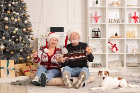 Foto de Pareja madura con bengalas navideñas y perro bebiendo champán en casa - Imagen libre de derechos