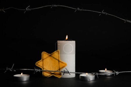 Velas ardientes con placa judía y alambre de púas sobre fondo oscuro. Día Internacional del Recuerdo del Holocausto
