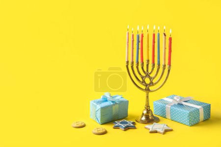 Photo for Menorah with cookies and gift boxes for Hanukkah celebration on yellow background - Royalty Free Image
