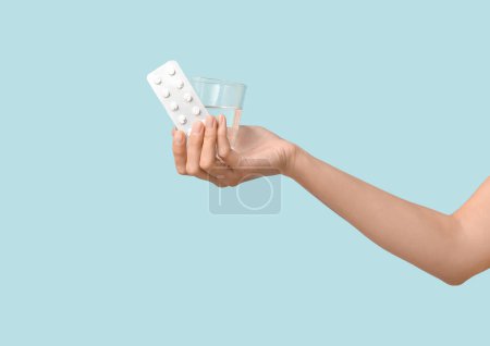 Téléchargez les photos : Main féminine avec pilules contraceptives et verre d'eau sur fond bleu. Concept de sexe sûr - en image libre de droit