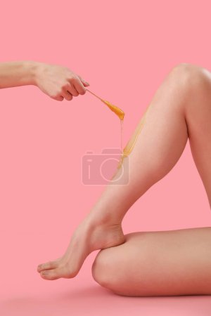 Foto de Mano que aplica la pasta de azúcar en las piernas de la mujer joven sobre fondo rosa - Imagen libre de derechos