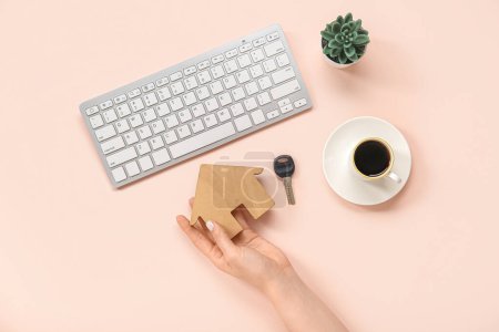 Téléchargez les photos : Main féminine avec figure de maison en bois, touche, clavier et café sur fond rose. Concept d'achat immobilier - en image libre de droit