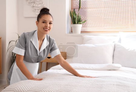 Schöne Zimmermädchen machen Bett im hellen Hotelzimmer