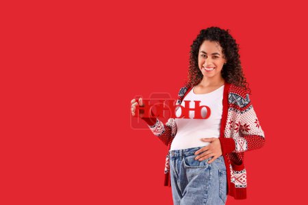 Téléchargez les photos : Femme afro-américaine enceinte avec salutation de Noël sur fond rouge - en image libre de droit