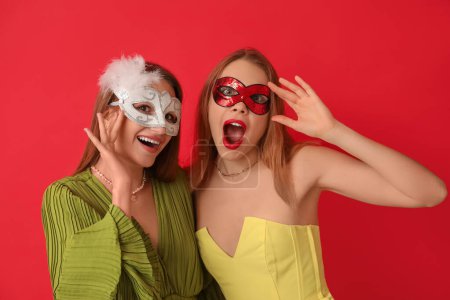 Téléchargez les photos : Jeunes femmes choquées dans des masques de carnaval sur fond rouge - en image libre de droit